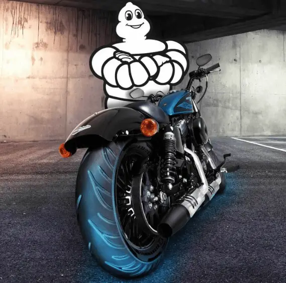 A Michelin Man standing behind a Harley Fat Bob with a Michelin Commander 3 installed